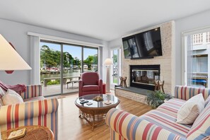 Una sala de estar con chimenea, televisor montado en la pared y un gran ventanal con vistas a un cuerpo de agua.