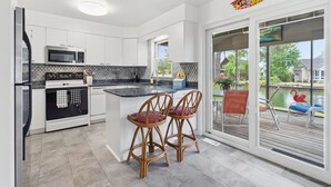 A modern kitchen with white cabinets, a black and white stove, and a large island with two bar stools. - Water's Edge Retreat OCMD (Ocean Pines)