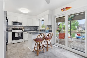 A modern kitchen with white cabinets, a black and white stove, and a large island with two bar stools. - Water's Edge Retreat OCMD (Ocean Pines)