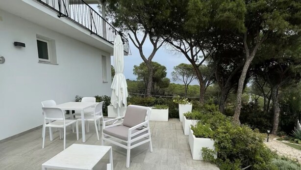 Une terrasse avec des meubles blancs, un parasol blanc et des plantes en pot.