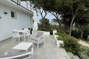 A patio with white furniture, a white umbrella, and potted plants. - Libeccio Apartment - Elegance and Relaxation 300 meters from the Sea (Santa Margherita di Pula)