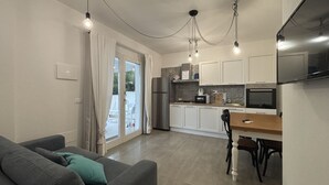 Une cuisine moderne avec des meubles blancs, une table à manger et un canapé agrémenté d’un coussin vert.