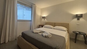 Une chambre d’hôtel avec un lit, deux tables de chevet, une fenêtre avec des rideaux et des lampes fixées au mur.