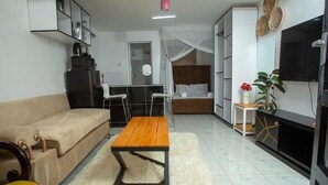 Een woonkamer met een bank, een houten salontafel, een televisie, een keukenhoek en een eettafel.