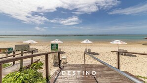 A beach view with a wooden deck, beach umbrellas, and a sign indicating amenities. - APTO Térreo | 4 Quartos | Até 12 Pessoas | Barra Bali | Destino BSM 002 (Barra de São Miguel)