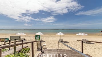 Na praia, areia branca, espreguiçadeiras, guarda-sóis