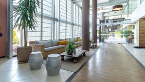 A spacious indoor area with a large window, a sofa with cushions, a coffee table, and decorative planters. - APTO Térreo | 4 Quartos | Até 12 Pessoas | Barra Bali | Destino BSM 002 (Barra de São Miguel)