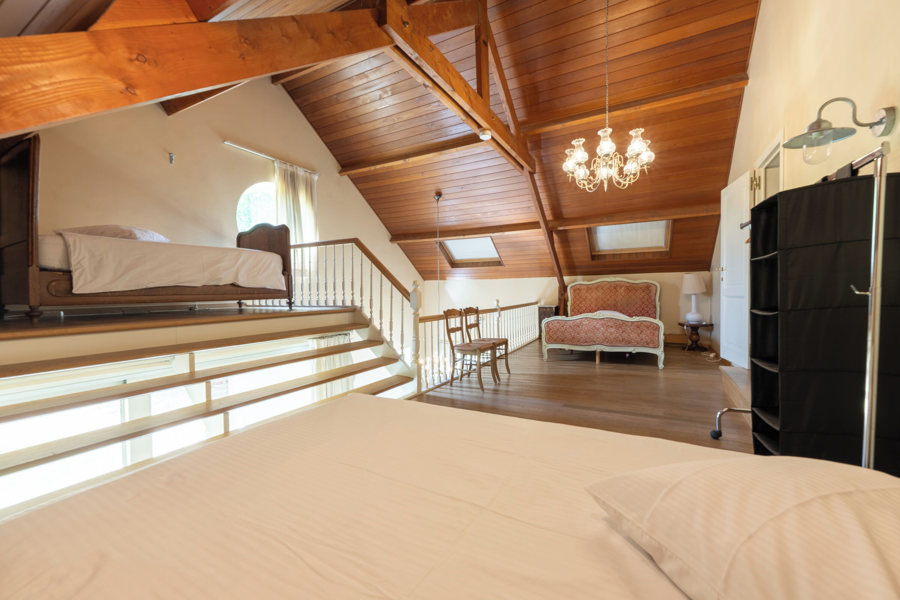 A bedroom with a large bed, a chair, a desk, and a wardrobe.