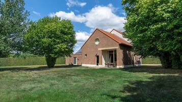A brick house with a sloped roof, a front door, and a small porch with chairs.