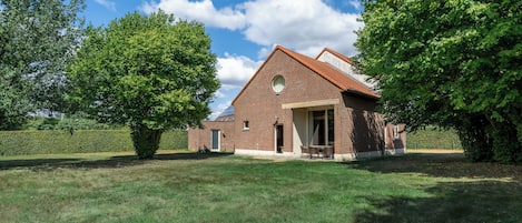 A brick house with a sloped roof, a front door, and a small porch with chairs.