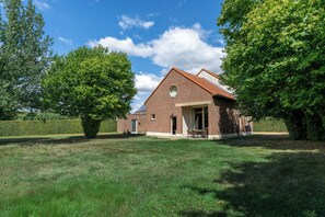 A brick house with a sloped roof, a front door, and a small porch with chairs. - Villa Krat (Holsbeek)