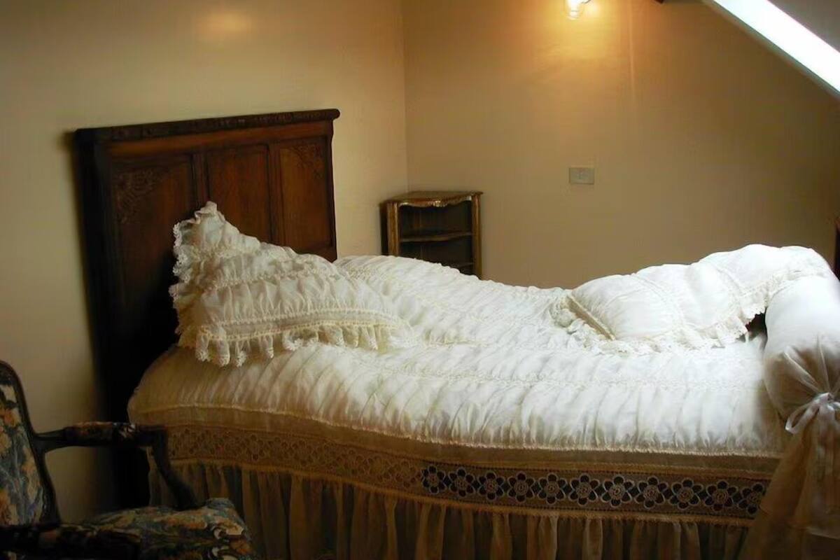 A bed with a wooden headboard, a small bedside table, and a chair with a patterned cushion.