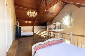 A bedroom with a wooden ceiling, a chandelier, a bed with a patterned headboard, a small table, and a window with curtains. - Villa Krat (Holsbeek)