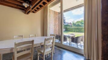 A dining area with a wooden table and chairs, a brick wall, and a view of a garden through a glass door.