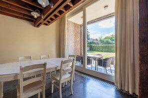 A dining area with a wooden table and chairs, a brick wall, and a view of a garden through a glass door. - Villa Krat (Holsbeek)