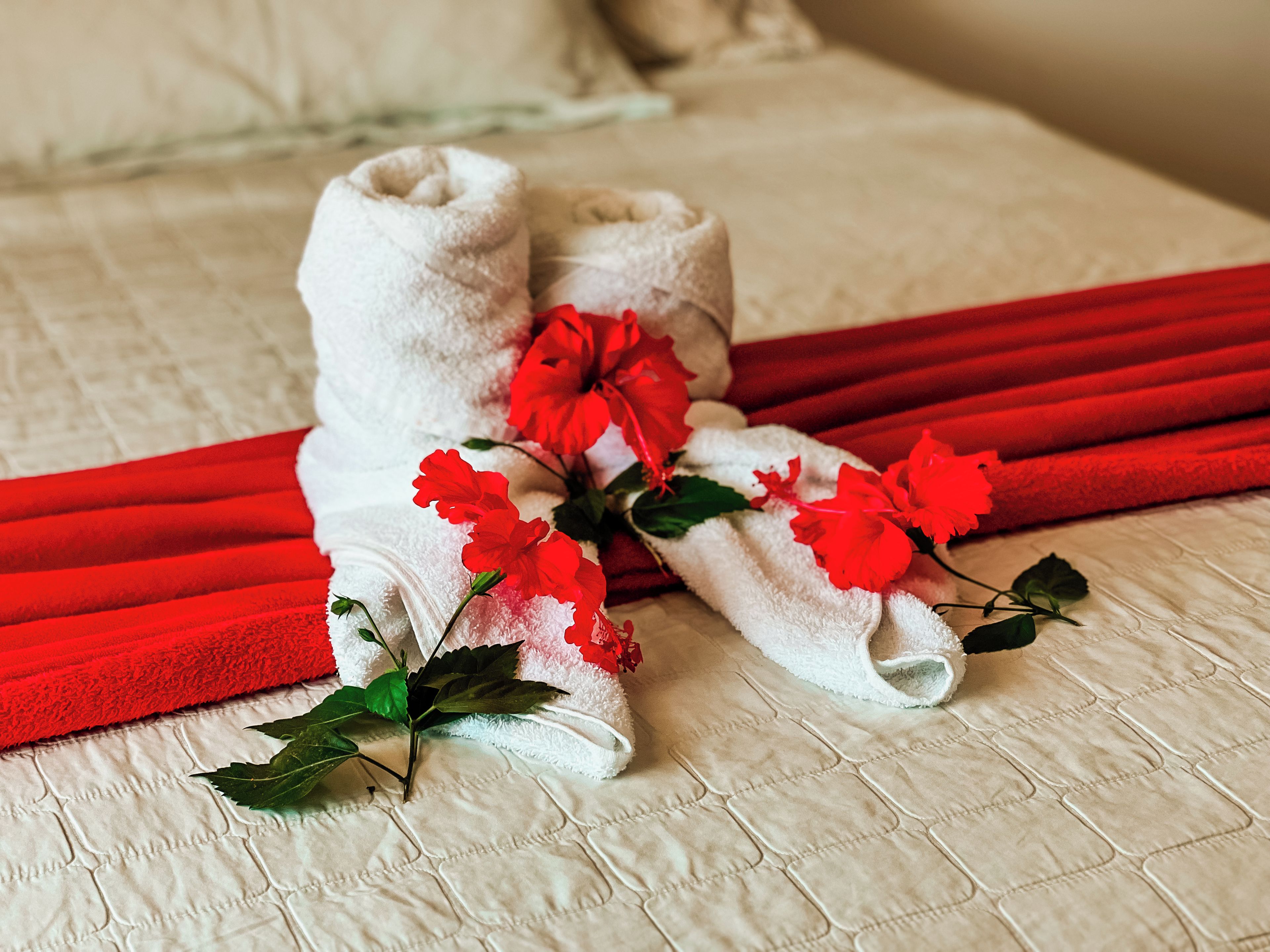 A neatly made bed with a white duvet, red decorative pillows, and a red ribbon.