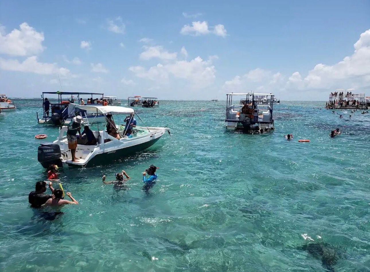 Un mar azul y transparente con barcos y gente nadando.