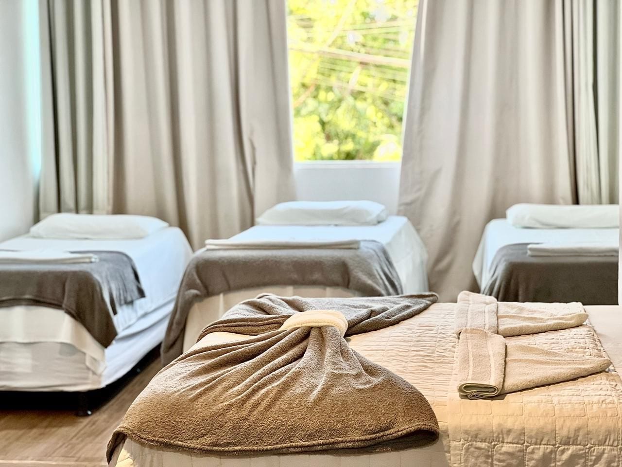 A hotel room with three beds, each with a towel and a blanket.