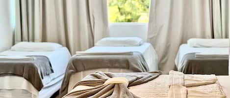 A hotel room with three beds, each with a towel and a blanket.