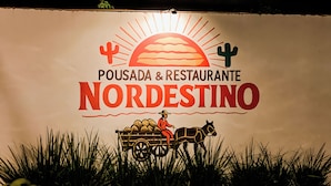 Ein Schild mit dem Text 'POUSADA & RESTAURANTE NORDESTINO' und einer Darstellung einer Person in einer von Pferden gezogenen Kutsche.