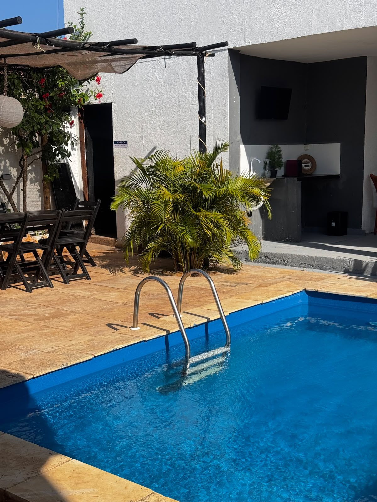 A swimming pool with a metal ladder, surrounded by a wooden deck and a white wall.