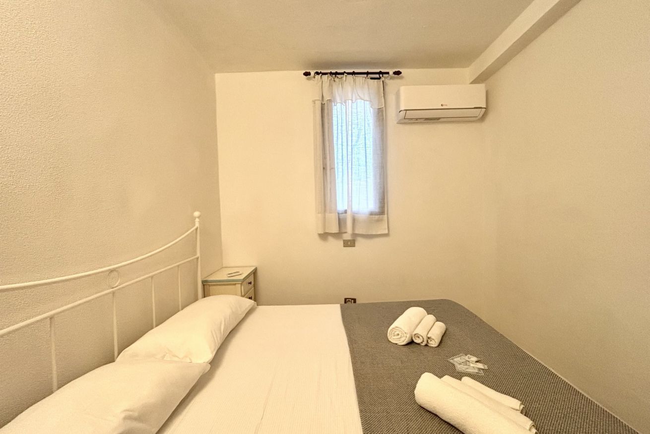 A single bed with a headboard, a bedside table, a window with a curtain, and an air conditioning unit on the wall.