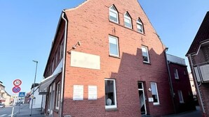 A red brick building with a flat roof and a large window on the ground floor. There are signs on the sidewalk indicating a 30 km/h speed limit and a no parking zone. - sleepWELL-Nordhorn II – Neu & Modern zentrale Lage (Nordhorn)