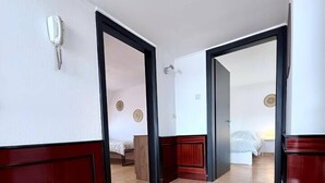 A hotel room with a wooden floor, a bed with a white cover, a nightstand, and a wall-mounted telephone. - sleepWELL-Nordhorn II – Neu & Modern zentrale Lage (Nordhorn)