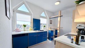 A modern kitchen with blue cabinets, a white countertop, and a window with a view of buildings. - sleepWELL-Nordhorn II – Neu & Modern zentrale Lage (Nordhorn)