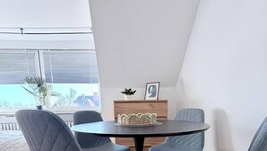 A modern dining area with a round table and four grey upholstered chairs. - sleepWELL-Nordhorn II – Neu & Modern zentrale Lage (Nordhorn)