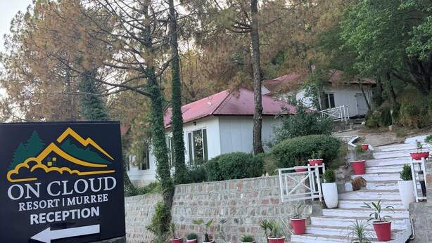 Señal para la recepción del On Cloud Resort Murree, con un gráfico de montaña, una pared de piedra y plantas en macetas rojas en los escalones.