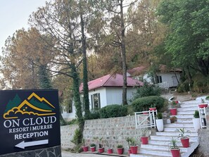 Schild für On Cloud Resort Murree Rezeption mit Bergmotiv, einer Steinmauer und roten Topfpflanzen auf Stufen.
