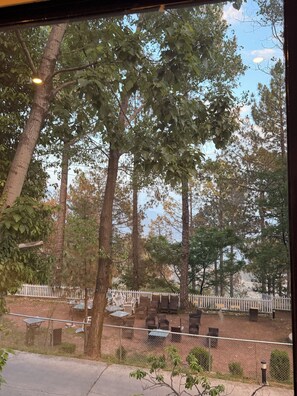 A view of a fenced outdoor area with tables and chairs, surrounded by trees. - On Cloud Resort (Murree)
