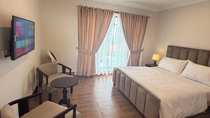 Una habitación de hotel con cama, escritorio, silla, televisor y ventana con cortinas.