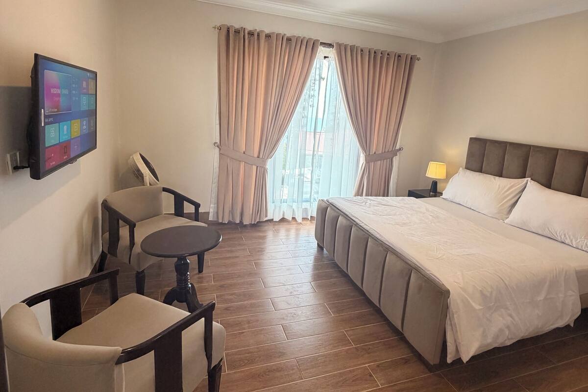 A hotel room with a bed, a desk, a chair, a TV, and a window with curtains.
