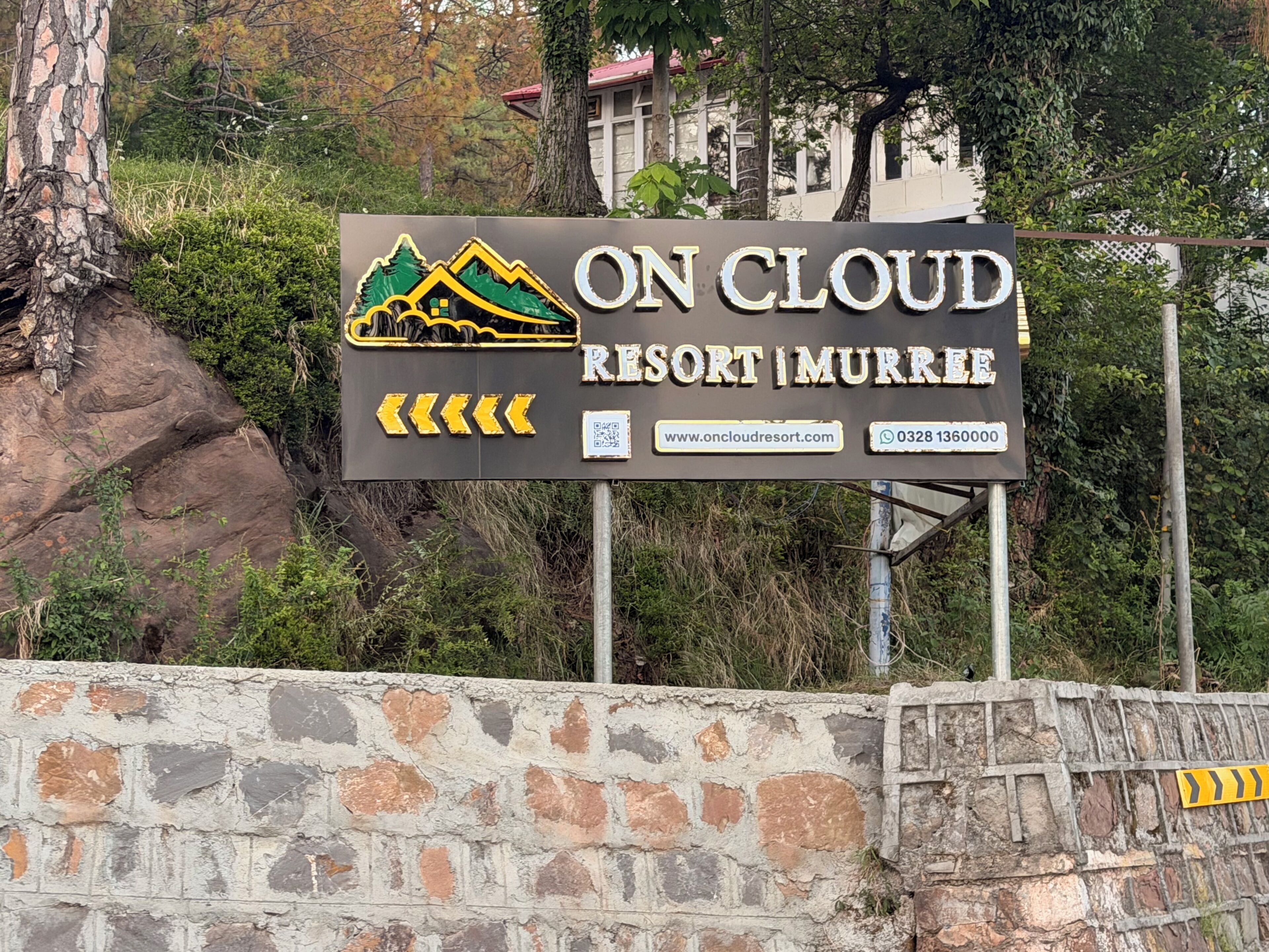 A sign for On Cloud Resort in Murree, featuring a mountain and house graphic, website, and contact number.