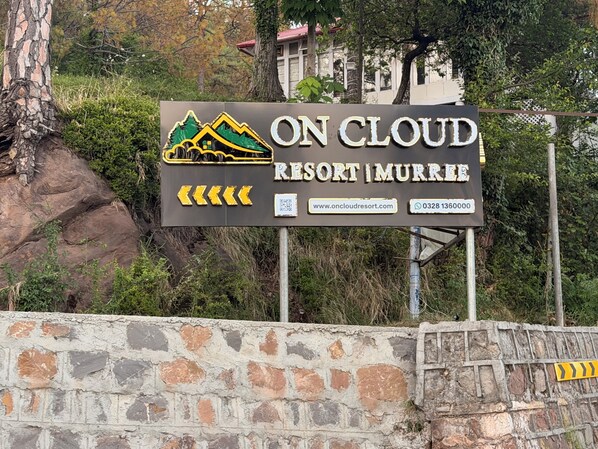 A sign for On Cloud Resort in Murree, featuring a mountain and house graphic, website, and contact number. - On Cloud Resort (Murree)