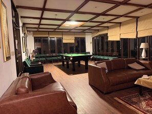 A billiards room with a pool table, leather sofas, and a patterned rug. - On Cloud Resort (Murree)