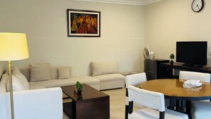 Una sala de estar con sofá, mesa de centro, comedor con sillas, televisor y un reloj en la pared.