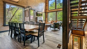 Un intérieur en bois comprenant un coin repas, une cheminée et de grandes fenêtres donnant sur l’extérieur.