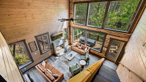 Une cabane dotée d’une cheminée en pierre, de planchers en bois et de grandes fenêtres donnant sur la forêt.