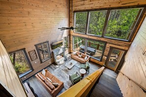 A cabin with a stone fireplace, wooden floors, and large windows offering forest views. - New! 5BR w/Pool*Hot Tub*Game Room*Location! (Sevierville)
