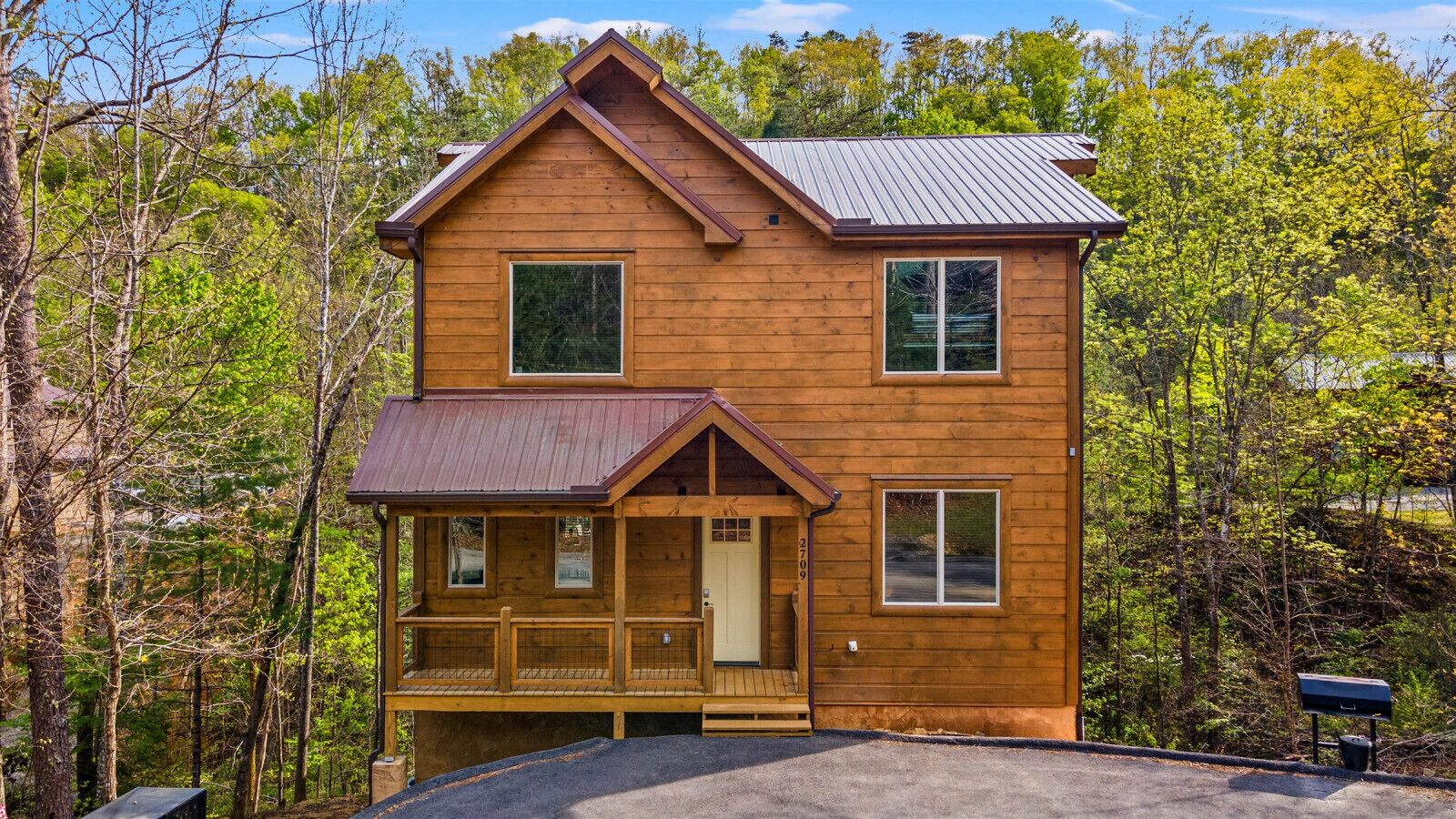 A two-story wooden cabin with a porch, surrounded by trees.
