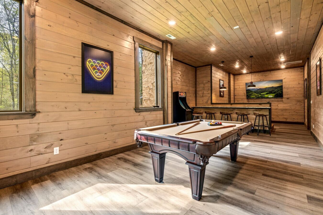 A pool table in a room with wooden walls and a bar area.