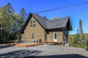Une cabane à deux étages, dotée d’un toit en pente, d’une terrasse avec des sièges et d’un petit abri attenant.