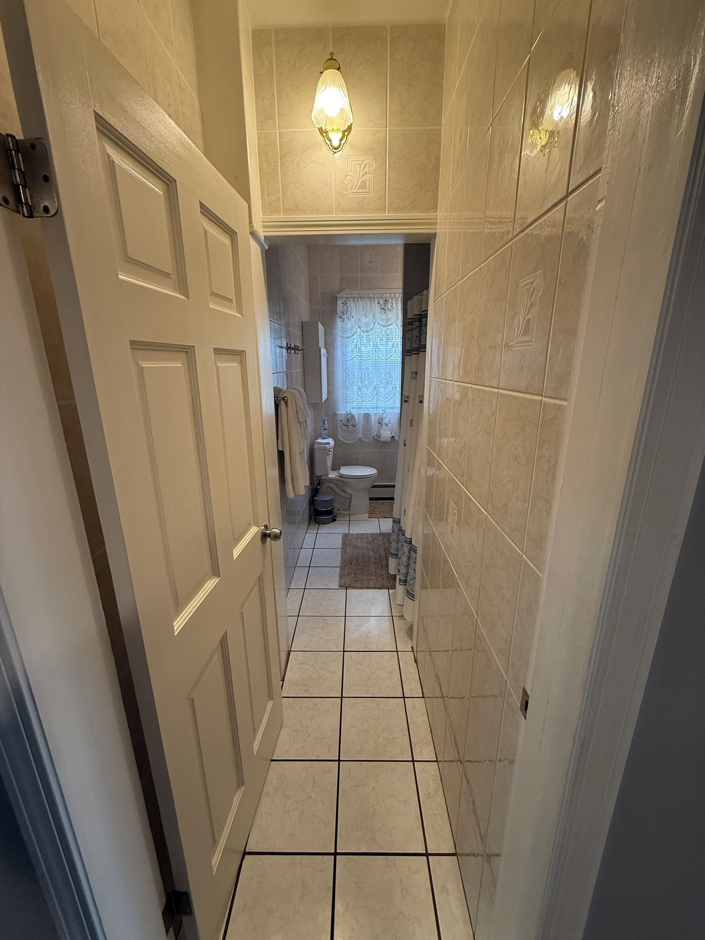 Un pasillo estrecho que conduce a un baño con inodoro, lavamanos y perchero.