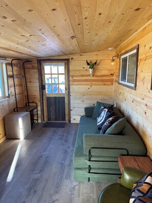 En mysig stuga med träpanel i taket, en grön soffa, ett litet bord och en väggmonterad lampa.