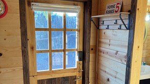 Interior de una cabaña de madera con un ventanal grande, una puerta con manija y un letrero que dice 'Horse Kisses 5'.
