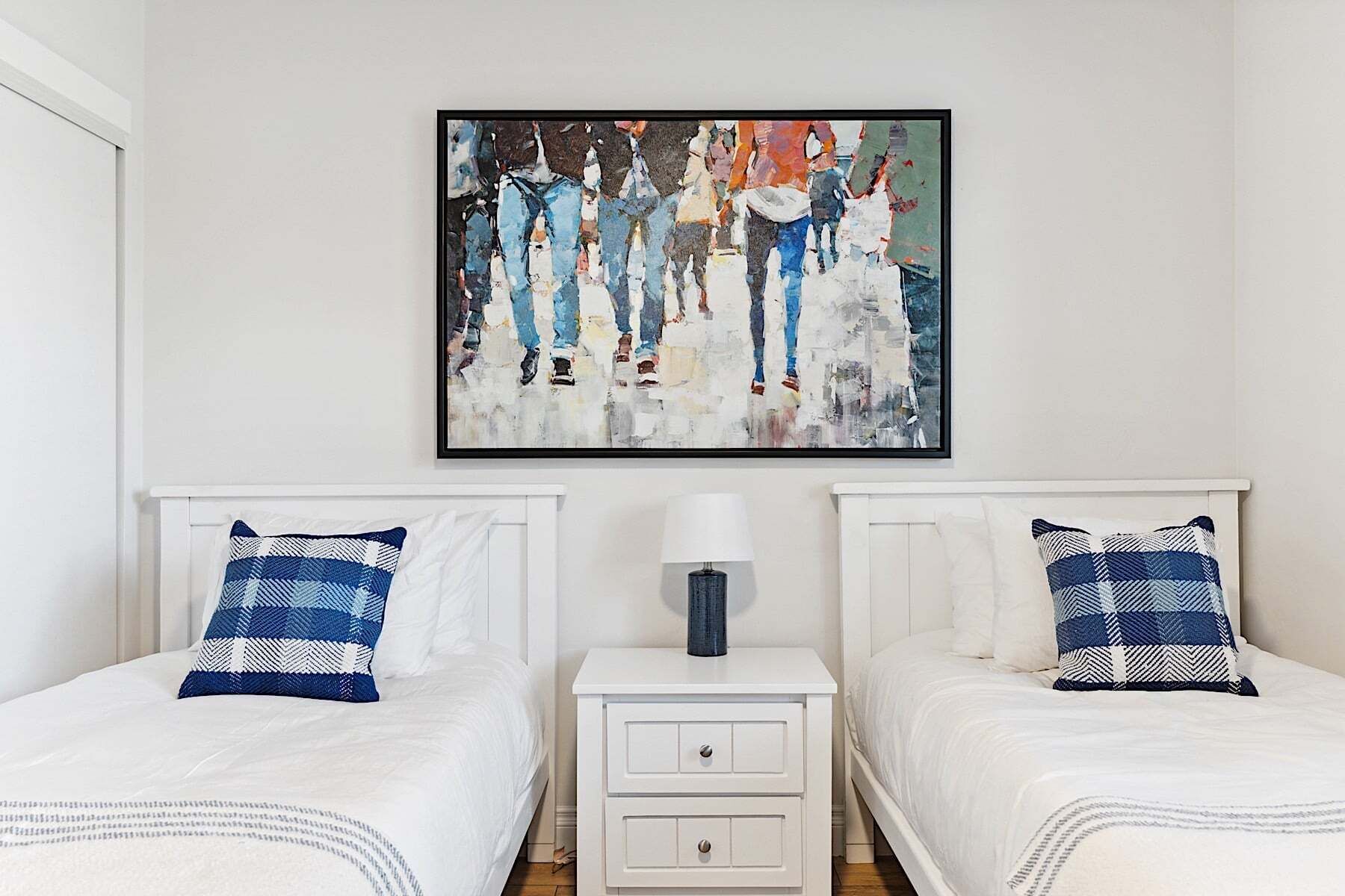 A bedroom with two beds, a nightstand with a lamp, and a painting on the wall.