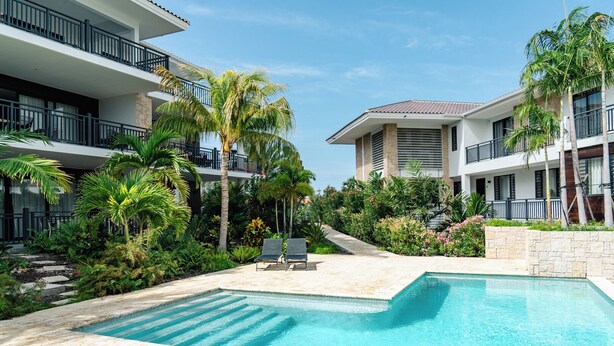 Un resort con piscina, palmeras y un edificio de dos pisos con balcones.